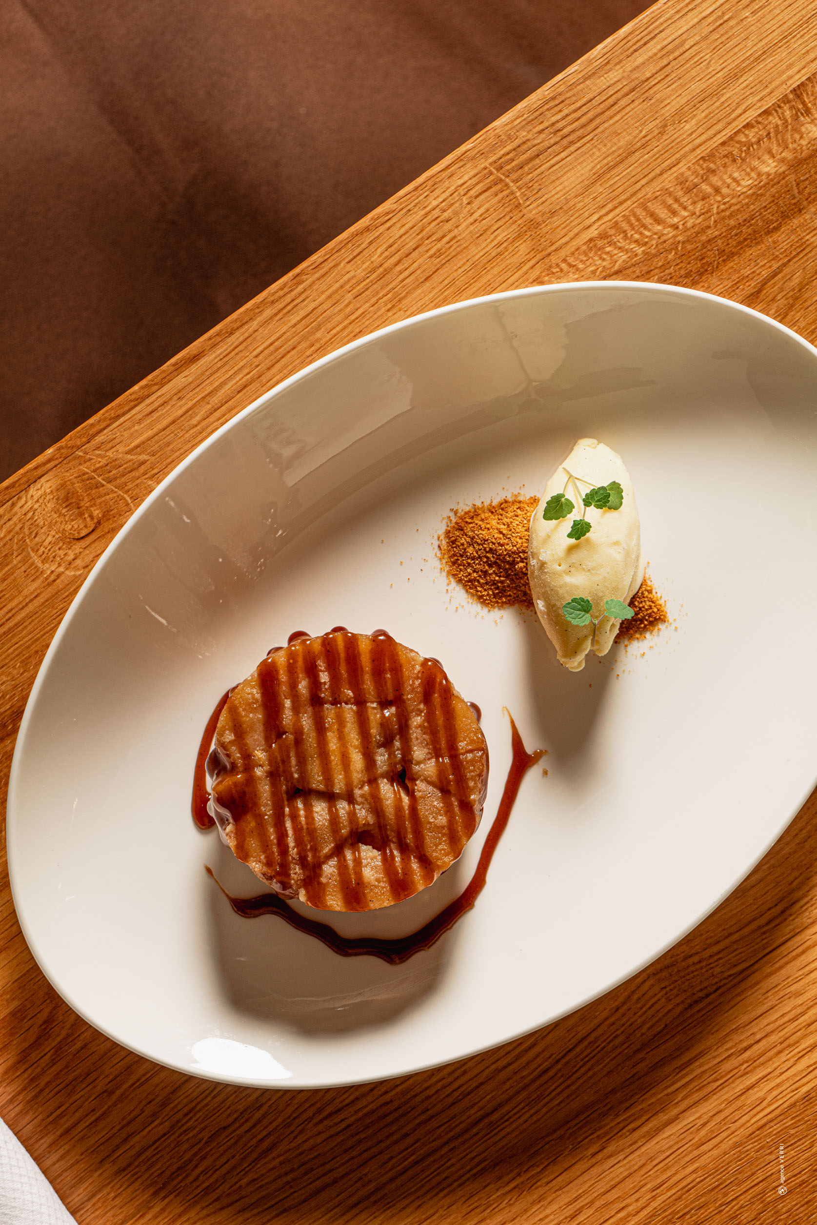 Dessert gastronomique dressé avec soin : gâteau moelleux nappé de caramel accompagné d’une boule de glace artisanale à la vanille, servi sur assiette blanche.